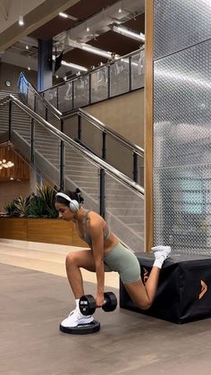 a woman is doing push ups in the middle of an indoor area with stairs and railings