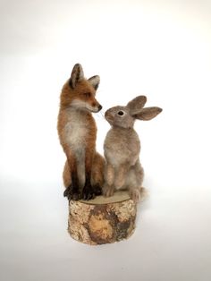 two small stuffed animals sitting on top of a wooden stump in front of a white background