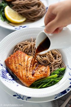 someone is pouring sauce on some food in a white bowl with noodles and asparagus