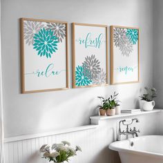 three framed pictures on the wall above a bathtub in a white bathroom with flowers