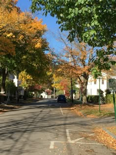 an empty street lined with houses and trees in the fall time, on a sunny day