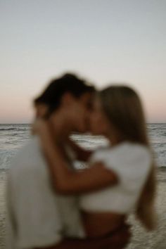 a man and woman kissing on the beach at sunset with waves in the background, blurry image