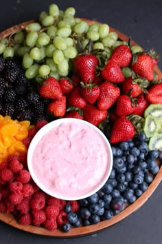 a platter filled with berries, grapes, kiwis and other fruits next to a small bowl of dip