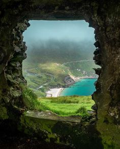 an open window in the side of a stone wall looking at a body of water