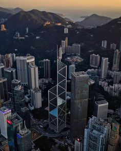 an aerial view of skyscrapers in the city with mountains in the background at sunset