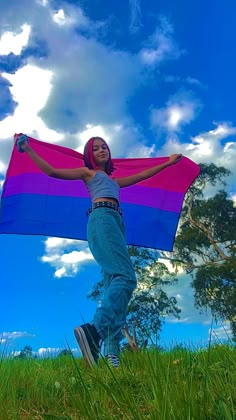 a woman standing on top of a lush green field holding a purple and blue kite