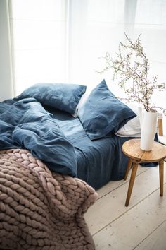 a bed sitting next to a window with blue sheets and blankets on top of it