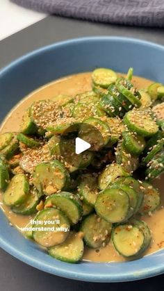 a blue bowl filled with cucumbers covered in sauce and sprinkled with sesame seeds