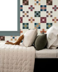 a bed topped with pillows next to a wall covered in colorful squares and shapes on it