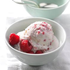 a bowl filled with ice cream and raspberries on top of a white table