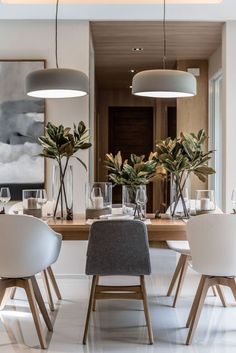 an elegant dining room with white chairs and wooden table surrounded by potted greenery