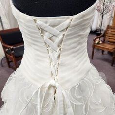 a white wedding dress on display in a room with chairs and other items behind it