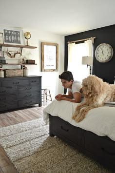 a person laying on a bed with a dog in front of them and a clock above the bed