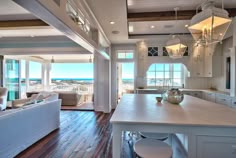 a large open concept living room and kitchen area with wood flooring, white furniture and an ocean view