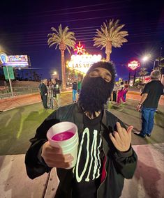 a man with a beard holding a cup in front of a neon las vegas sign