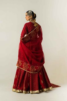 a woman in a red and gold lehenga is standing with her back to the camera