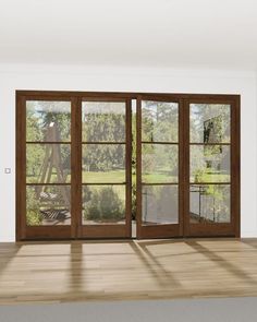 an empty room with wooden floors and sliding glass doors that lead to a large garden