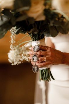 a woman in a white dress holding a bouquet of flowers and two rings on her hand