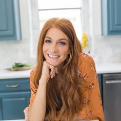 a woman with long red hair sitting at a table in a kitchen smiling for the camera