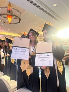 two women in graduation gowns holding up their diplomas