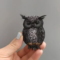 an owl figurine sitting on top of someone's finger in front of a gray wall