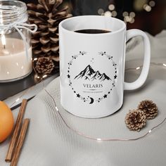 a white coffee mug sitting on top of a table next to an orange and pine cone