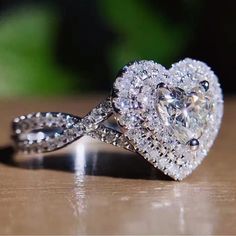 a heart shaped diamond ring sitting on top of a wooden table