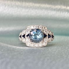 A magnificent 1.21-carat round-cut aquamarine is placed in prongs on a geometric gemstone ring. The aquamarine ring is flanked by a row of triangular French cut sapphires, which are also set on the stepped shoulders. Around the shoulders and set around the sapphires and aquamarine are round brilliant cut diamonds.  This ring contains roughly 0.45 carats of diamonds in total. The total carat weight of the sapphires is approx 0.22 handcrafted in a platinum ring that features an openwork under-gall Gia Certified Blue Art Deco Jewelry, Blue Art Deco Jewelry Gia Certified, Aquamarine Gemstone Diamond Ring In Round Cut, Aquamarine Diamond Ring With Round Cut, Light Blue Round Cut Diamond Jewelry, Luxury Light Blue Round Ring, Luxury Light Blue Round Rings, Aquamarine Diamond Ring With Gemstone Detail, Round Aquamarine Diamond Ring With Gemstone