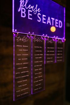 a sign that says please be seated on the side of a building with purple lights