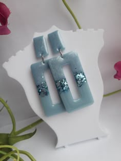 two square shaped earrings with blue and silver sequins on them sitting on a white surface