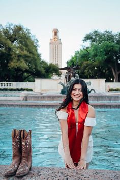 a woman sitting on the edge of a fountain with her boots in front of her