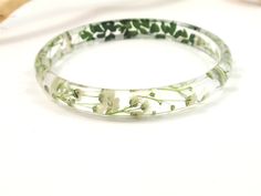 a close up of a bracelet on a white surface with green and white flowers in it