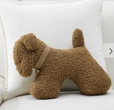 a brown dog pillow sitting on top of a white couch next to a stuffed animal