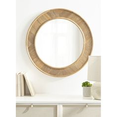 a round mirror sitting on top of a white shelf next to a lamp and book