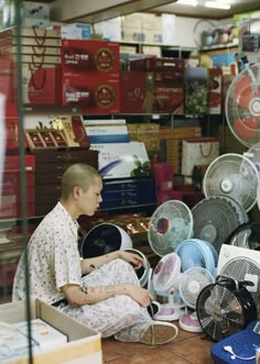 a man sitting on the floor in front of many fan's and other items