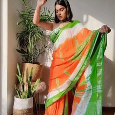 a woman in an orange and green sari standing next to a potted plant