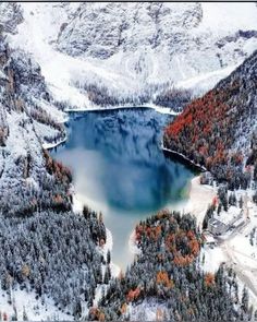 an aerial view of a mountain lake surrounded by trees and snow covered mountains in the background