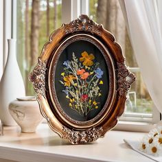 an ornate gold frame with flowers painted on the inside is sitting on a window sill