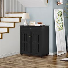 a black cabinet sitting in the corner of a room next to a mirror and stairs