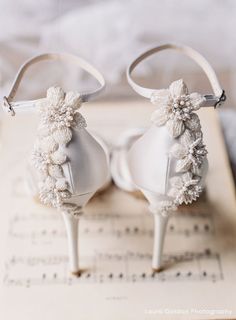 two white shoes with bows and pearls on them sitting on top of an open book