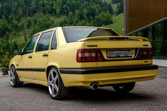 the rear end of a yellow car parked in a parking lot next to a building