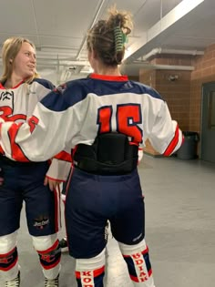 two female ice hockey players standing next to each other in an indoor rink with their arms around one another