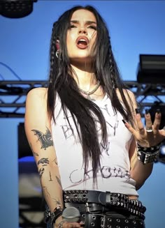 a woman with long black hair and piercings on her chest is singing into a microphone