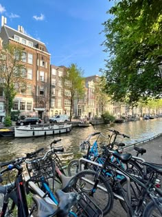 several bicycles parked next to each other on the side of a river with buildings in the background