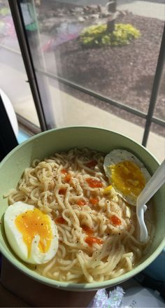 a bowl filled with noodles and eggs on top of a table next to a window