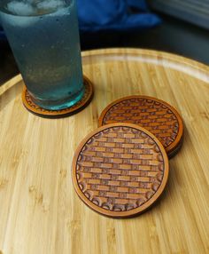 two coasters sitting on top of a wooden table next to a glass filled with water