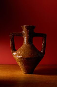 a brown vase sitting on top of a wooden table next to a red painted wall