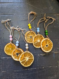 three orange slices are hanging from twine strings on a wooden surface, with beads around them