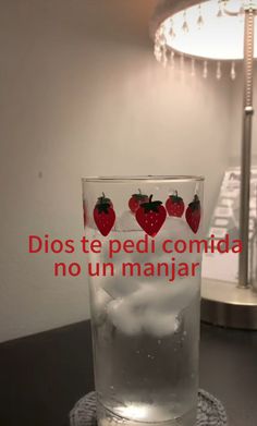 a glass filled with water and strawberries sitting on top of a table next to a lamp