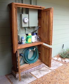 an open wooden box on the side of a house with hoses and other items in it